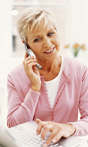 An old lady talking on mobile phone and working on a laptop