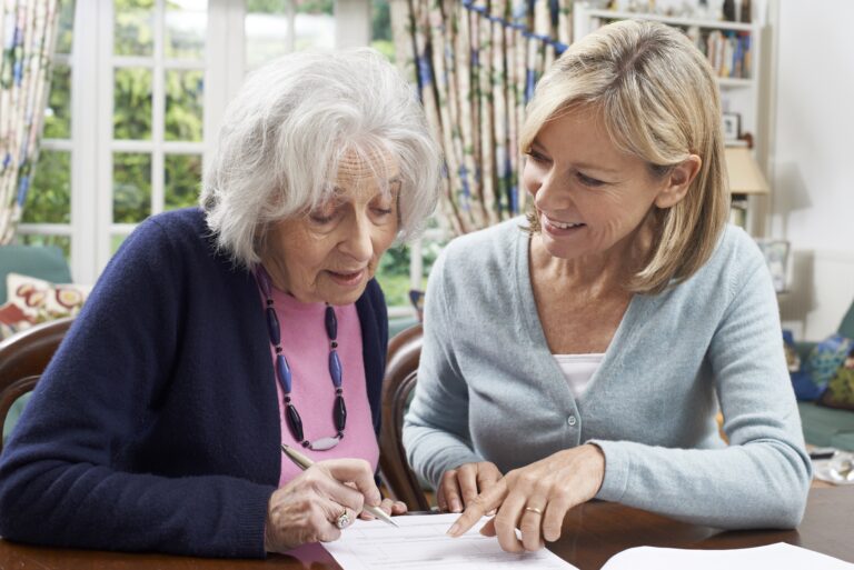 A woman signing a document with an older woman at a table.